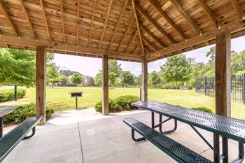 A wooden pavilion with green benches and a fence in the background.